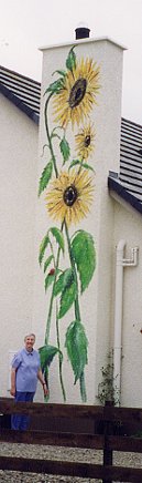 Angela standing below 21 ft high painted sunflower